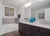 Thumbnail 8 of 36 - A bathroom with a white tub, brown cabinets, and a painting on the wall.