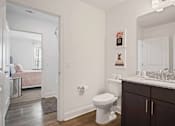 Thumbnail 10 of 36 - A white toilet sits in a bathroom with a wooden floor and white walls.