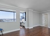 Thumbnail 12 of 32 - A room with a window overlooking a cityscape and a wooden floor.
