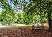 Thumbnail 19 of 23 - A park with a table and chairs under a tree.