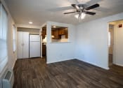 Thumbnail 10 of 16 - an empty living room with a ceiling fan and a kitchen in the background