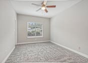 Thumbnail 31 of 36 - A room with a ceiling fan and carpeted floor.
