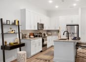 Thumbnail 5 of 46 - Apartments in Norcross, GA for Rent - The Darnell - White Kitchen with Cooking Island with Seating, Silver Appliances, Granite Sandy Countertops, White Cabinets, and Silver Hardware