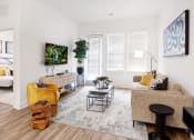 Thumbnail 8 of 46 - Apartments for Rent in Norcross GA - The Darnell - Furnished Living Room with Sofa, Mounted TV and Monitor with Storage, Armchairs, Carpet, Side Tables, Lamps, Houseplant, and Windows
