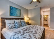 Thumbnail 4 of 34 - 1 BR Apartments in Maitland, FL - Parker at Maitland - Furnished Bedroom with Carpeted Floor, Large Bed, Ceiling Fan, Framed Art, Wooden Nightstand with Lamp, and Attached Bathroom