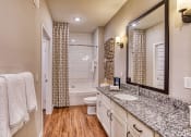 Thumbnail 6 of 34 - 1-Bedroom Apartments in Maitland, FL - The Parker at Maitland Station - Bathroom with Wood Vinyl Plank Flooring, Double Sink Vanity, Granite Countertop, Wood-Tone Flat-Panel Cabinetry, and Tiled Shower/Tub Combo.