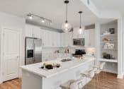 Thumbnail 1 of 58 - Buckhead, GA, Luxury Apartments Near Chastain Park - 92 West Paces - Modern Kitchen with Hardwood Flooring, White Maple Cabinetry with Stainless Steel Pulls, White Quartz Countertops, Large Cooking Island/Breakfast Bar, Bar-Style Chairs, Pendant and Track Lights, Stainless Steel Appliances, and Display Shelves.