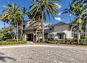 Thumbnail 2 of 53 - A house with a driveway and palm trees in front.