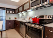 Thumbnail 23 of 39 - Orlando, FL Pet-Friendly Luxury Apartments - NORA - Kitchen with Moveable Island, Stainless Steel Appliances, Wood-Tone Cabinetry, and White Granite Countertops.
