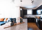 Thumbnail 11 of 36 - Greenville SC Pet Friendly Apartments - Velo Verdae - Modern Kitchen with Natural Oak-Style Plank Flooring, Stainless Steel Appliances, White tile Backsplash, Granite Countertops, Cooking Island, Dark Wood Cabinetry, and Overhead Lighting