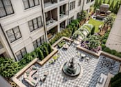 Thumbnail 15 of 16 - A courtyard with a fountain and seating area surrounded by buildings.