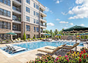 Thumbnail 16 of 16 - A large swimming pool with sun loungers and umbrellas in front of a multi-story apartment building.