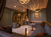 Thumbnail 7 of 16 - A modern living room with a grey sofa, a round table, and a chandelier.