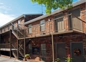Thumbnail 7 of 16 - an exterior view of a brick apartment building with a wooden balcony