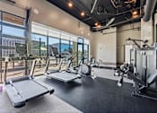 Thumbnail 9 of 34 - Pet-Friendly Luxury Apartments in Huntsville, AL - The Arcadia - Fitness Center with Treadmills, Elliptical Machines, Stationary Bike, Weight Lifting Equipment, High Ceiling with Exposed Piping, Ceiling Fan, and Window Wall with View of Pool Area.