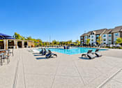 Thumbnail 20 of 29 - A large outdoor swimming pool with sun loungers and a building in the background.