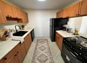Thumbnail 3 of 15 - Dog-Friendly Luxury Apartments In Hollywood, FL - Park Hill Hollywood - A Modern Kitchen With Tile Flooring, Wood Cabinetry, Granite Countertops, And Black Appliances.