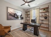 Thumbnail 41 of 65 - A room with a brown chair, a desk, and a painting of a vintage car on the wall.