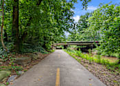 Thumbnail 34 of 38 - A pathway with a yellow line in the middle leads to a bridge over a river.