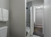 Thumbnail 12 of 38 - A bathroom with a toilet, a shower curtain, and a doorway leading to another room.