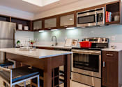 Thumbnail 22 of 39 - Luxury Apartments in Orlando, FL, with In-Unit Washer and Dryer - NORA - Kitchen with a Moveable Island, Bar Stools, White Quartz Countertops, Dark Wood Cabinetry, and Stainless Steel Appliances.