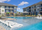 Thumbnail 12 of 28 - Luxury Apartments for Rent in Huntsville AL - The Kelvin - Gated Sparkling Pool with Sundeck, Submerged and Poolside Lounge Seats, Umbrellas, and View of Building Exterior in Background