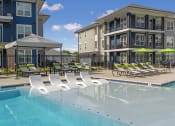 Thumbnail 11 of 28 - a swimming pool with lounge chairs and umbrellas in front of apartment buildings