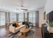 Thumbnail 8 of 21 - Studio Apartments in Chattanooga, TN - Populus Waterside - Living Room with Luxury Vinyl Tile Flooring, Area Rug, Sofa, Armchair, Coffee Table, Media Console, Wall-Mounted TV, Ceiling Fan, and Large Windows with Blinds.
