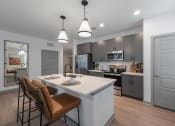 Thumbnail 5 of 21 - Studios in Chattanooga, TN - Populus Waterside - Kitchen with General Electric Stainless Steel Appliances, Quartz Countertops, Tile Backsplash, Kitchen Island/Breakfast Bar, Bar-Style Chairs, Pendant Lights, and Luxury Vinyl Tile Flooring.
