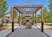 Thumbnail 23 of 29 - A wooden pergola with a table and chairs underneath it.