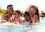 Thumbnail 2 of 41 - A family of four is enjoying a swim in a pool.