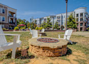 Thumbnail 47 of 53 - A fire pit sits in the middle of a grassy area with white chairs around it.