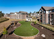 Thumbnail 44 of 45 - A large grassy area with a playground and apartment buildings in the background.