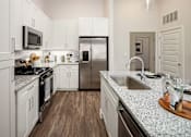 Thumbnail 10 of 45 - Two-Bedroom Luxury Apartments in Cumming, GA - Aura Creekside - Modern White Kitchen With Granite Island And Undermount Sink, Stainless Steel Refrigerator And Microwave.