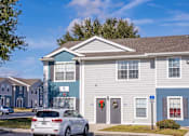Thumbnail 10 of 15 - A white car is parked in front of a grey and blue building.
