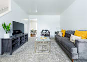 Thumbnail 5 of 18 - A living room with a grey couch and a glass coffee table.