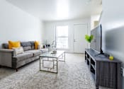 Thumbnail 4 of 18 - A living room with a grey couch, a coffee table, and a television.