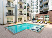 Thumbnail 51 of 57 - Two-Bedroom Apartments in Decatur, GA - Arlo Decatur - Resort-Style Pool With Poolside and In-Pool Lounge Seats, Umbrella, and View of Apartment Buildings