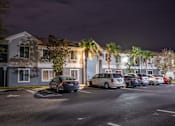 Thumbnail 38 of 43 - A parking lot with cars and a building with lights on in the background.
