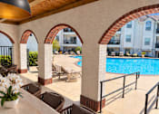 Thumbnail 6 of 20 - A pool area with chairs and a table with flowers.
