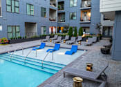 Thumbnail 27 of 31 - an apartment pool with blue lounge chairs in front of an apartment building