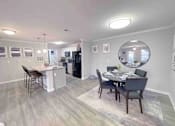 Thumbnail 11 of 24 - A dining room with a table set for two and a kitchen area in the background.