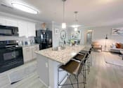 Thumbnail 10 of 24 - Greenville, SC, Luxury Apartments Near Falls Park On The Reedy - The Aventine Greenville - A Modern Open-Concept Kitchen With A Large Granite-Topped Island, White Cabinets, And Black Appliances.