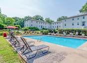 Thumbnail 4 of 18 - a swimming pool with chaise lounge chairs and a building in the background at Avondale Station Apartments, Georgia