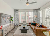 Thumbnail 17 of 30 - Fort Worth, TX, Luxury Apartments with In-Unit Washer and Dryer - The Union at River East - Living Room with a Brown Couch, Two Armchairs, Long Coffee Table, Cabinet, Ceiling Fan, and Floor Lamp.