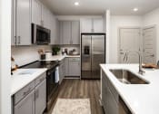 Thumbnail 5 of 70 - Apartments in Belmont, NC - The Banks Apartments - Gourmet Kitchen with Wood-Inspired Plank Flooring, Stainless-Steel Appliances, Quartz Countertops, Subway Tile Backsplash, and Grey Cabinets.