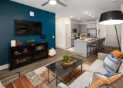 Thumbnail 6 of 70 - Apartments in Belmont for Rent - Banks at Mt. Holly - Open-Concept Living Room with Wood-Inspired Plank Flooring, Area Rug, Couch, Coffeetable, Floor Lamp, Wooden Media Consule, Ceiling Fan, and Access to Kitchen Area