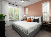 Thumbnail 9 of 70 - One-Bedroom Apartments in Belmont, NC - Banks at Mt. Holly - Bedroom with Carpeted Floor, Large Bed, Nighstands with Lamps, Dresser, Large Windows with Blinds and Curtains, and Ceiling Fan