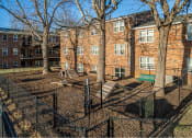 Thumbnail 6 of 16 - a fenced in area with a bench and trees in front of a brick building