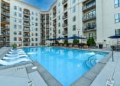 Thumbnail 35 of 58 - an outdoor swimming pool with lounge chairs and umbrellas in front of an apartment building